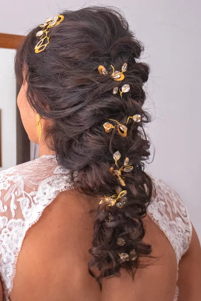 Penteado de noiva visto de costas: trança solta e volumosa com pequenos ganchos dourados.